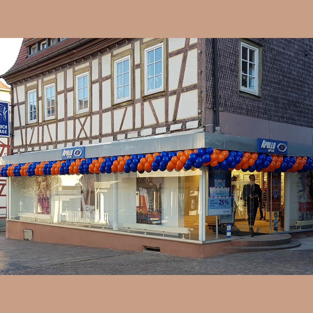 Fachwerkhaus in Michelstadt, das die neue Apollo-Optik Filiale beherbergt. Eine imposante Ballongirlande in den Firmenfarben Orange und Blau schmückt die gesamte Hausfront und beeindruckt jeden Passanten.